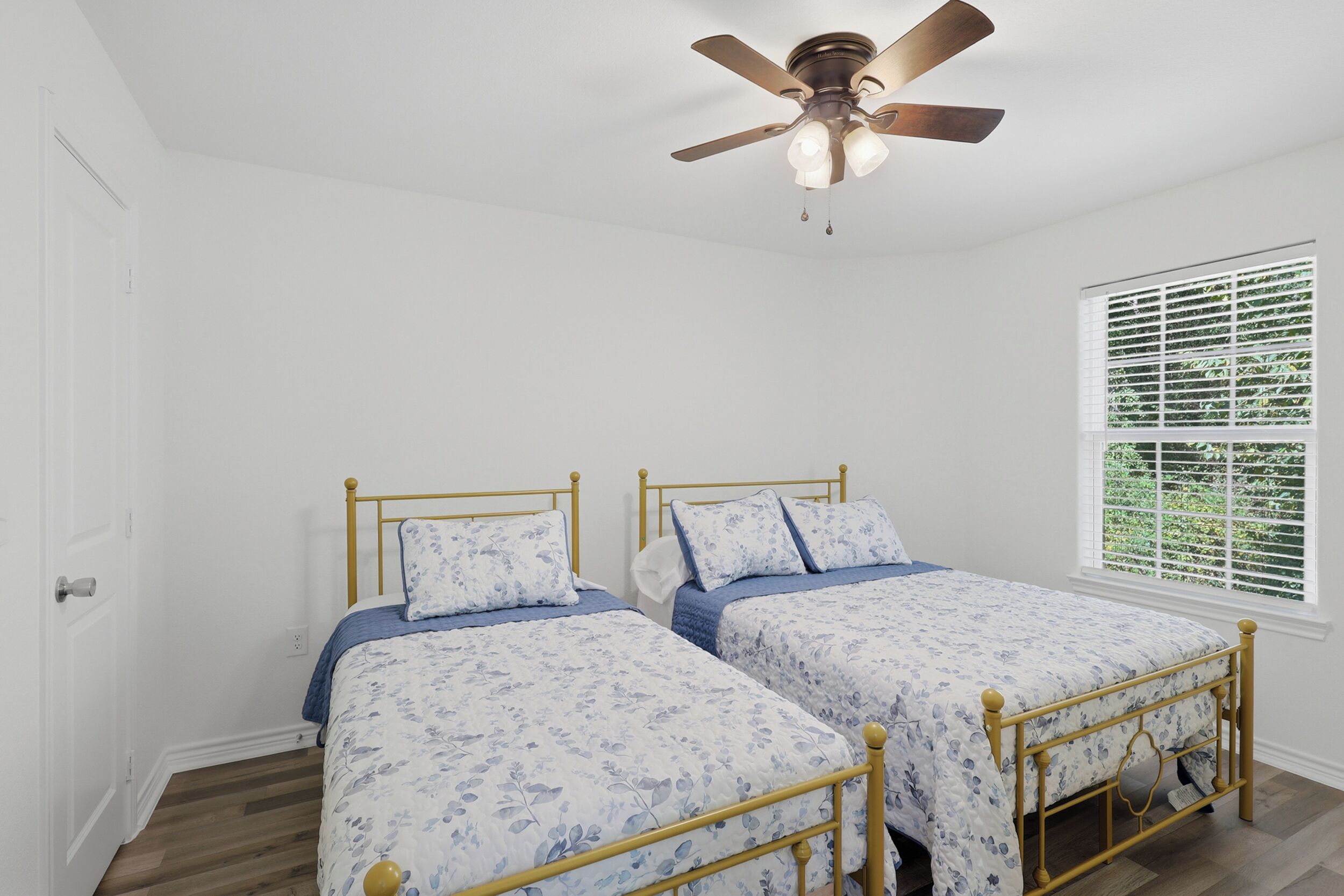 A bedroom with two single beds, a ceiling fan, and a window with blinds.