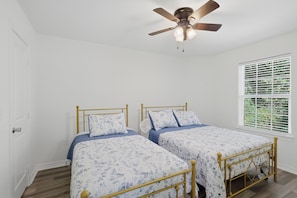 A bedroom with two single beds, a ceiling fan, and a window with blinds.