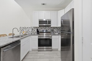 A kitchen with white cabinets, a stainless steel refrigerator, a microwave, an oven, and a sink with a faucet.