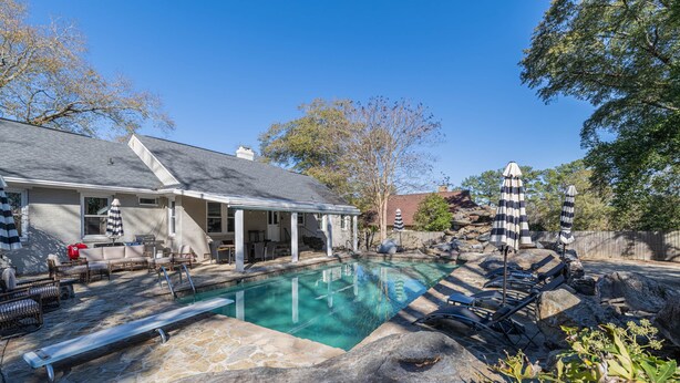 A residential swimming pool with lounge chairs and umbrellas, surrounded by a stone deck and a house. - Stone Pool House - Sleeps 8 (Columbus)