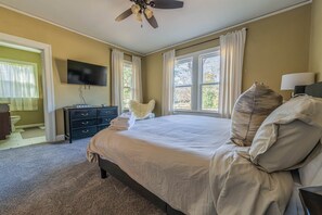 A bedroom with a large bed, a flat-screen TV mounted on the wall, and a ceiling fan. - Stone Pool House - Sleeps 8 (Columbus)