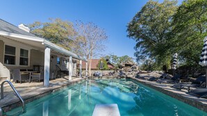 A swimming pool with a stone deck, lounge chairs, and a covered patio area with outdoor furniture. - Stone Pool House - Sleeps 8 (Columbus)