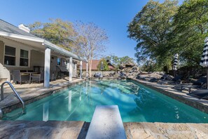 A swimming pool with a stone deck, lounge chairs, and a covered patio area with outdoor furniture. - Stone Pool House - Sleeps 8 (Columbus)