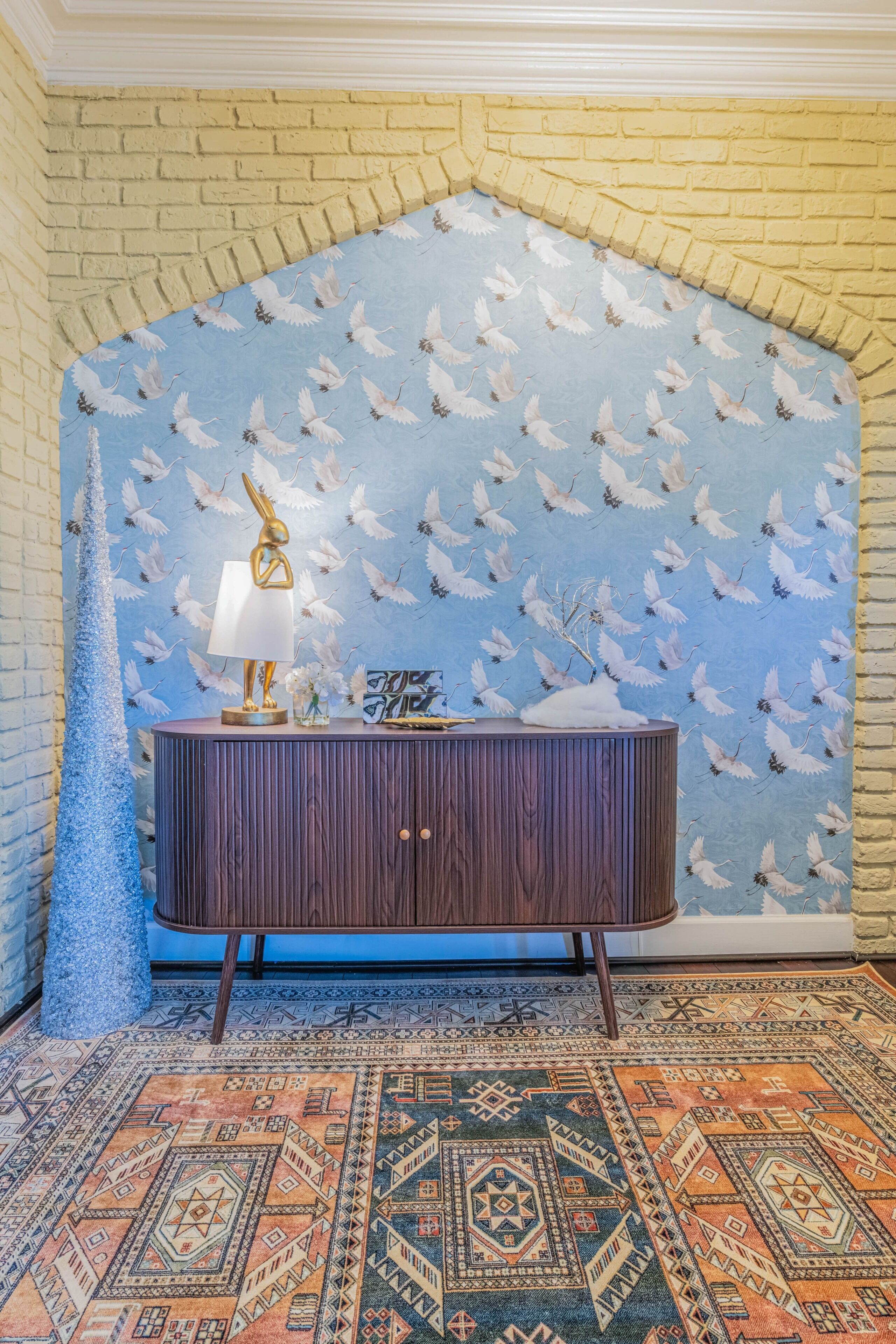 A room with a patterned wallpaper, a wooden cabinet, and a patterned rug.
