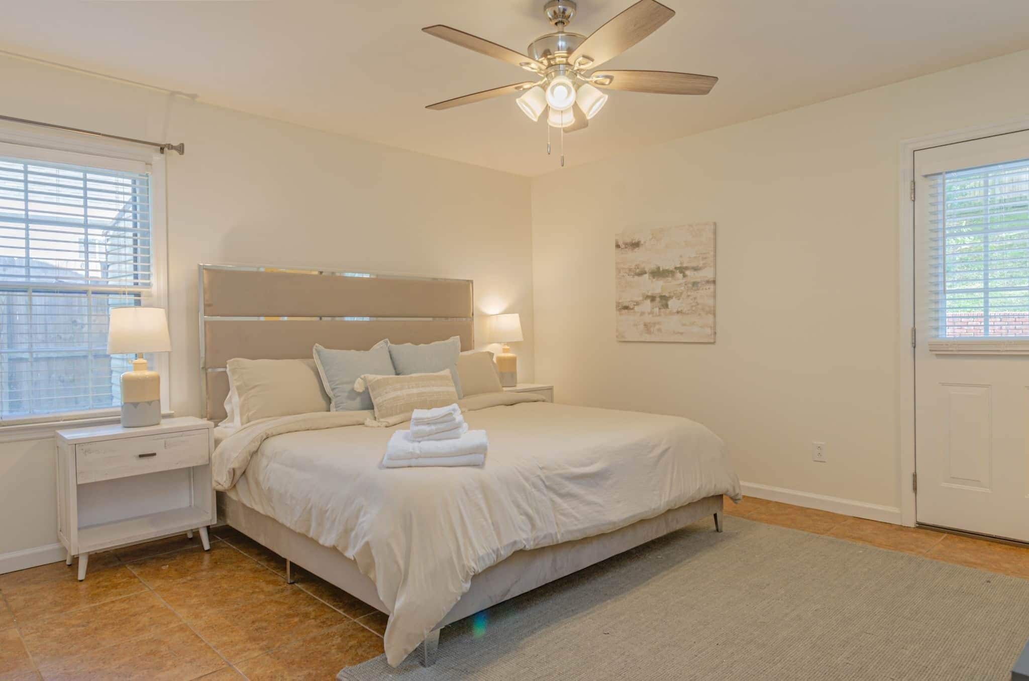 A bedroom with a bed, nightstands, a ceiling fan, and a window with blinds.