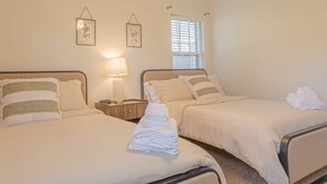 Quarto de hotel com duas camas, mesa de cabeceira, abajur e janela com persianas.