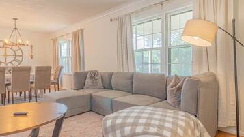 A modern living room with a sectional sofa, a round dining table, and a floor lamp.