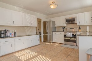 A modern kitchen with white cabinets, stainless steel appliances, and a tiled floor.
