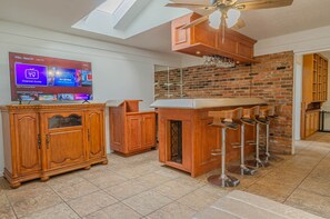 A modern kitchen with a brick wall, wooden cabinets, and a bar area with stools.