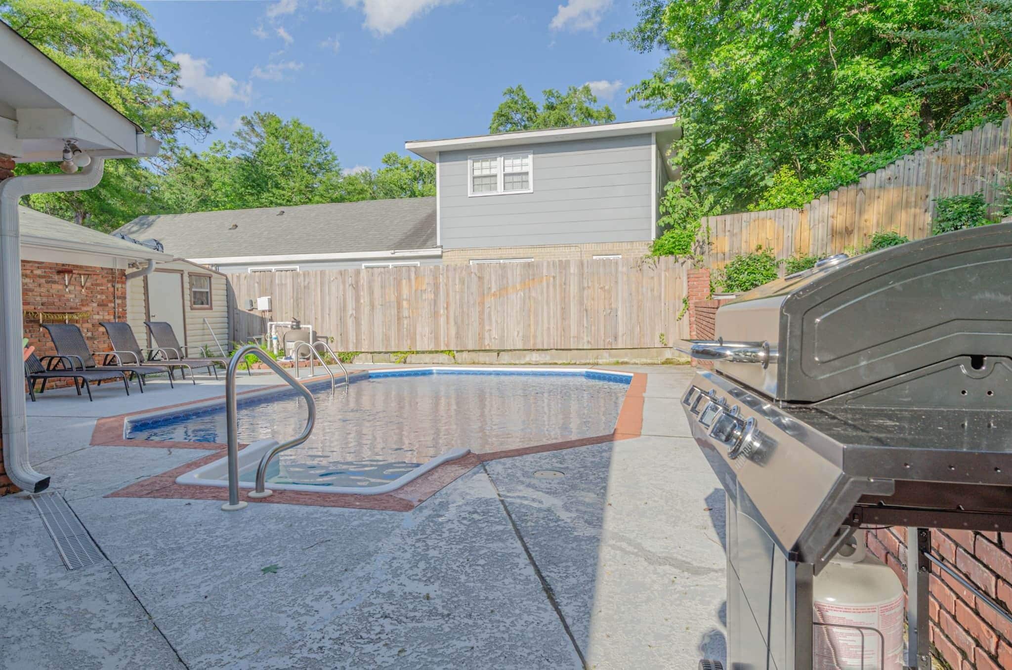 Un jardin avec une piscine, un barbecue et un espace patio couvert.