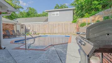 Un jardin avec une piscine, un barbecue et un espace patio couvert.