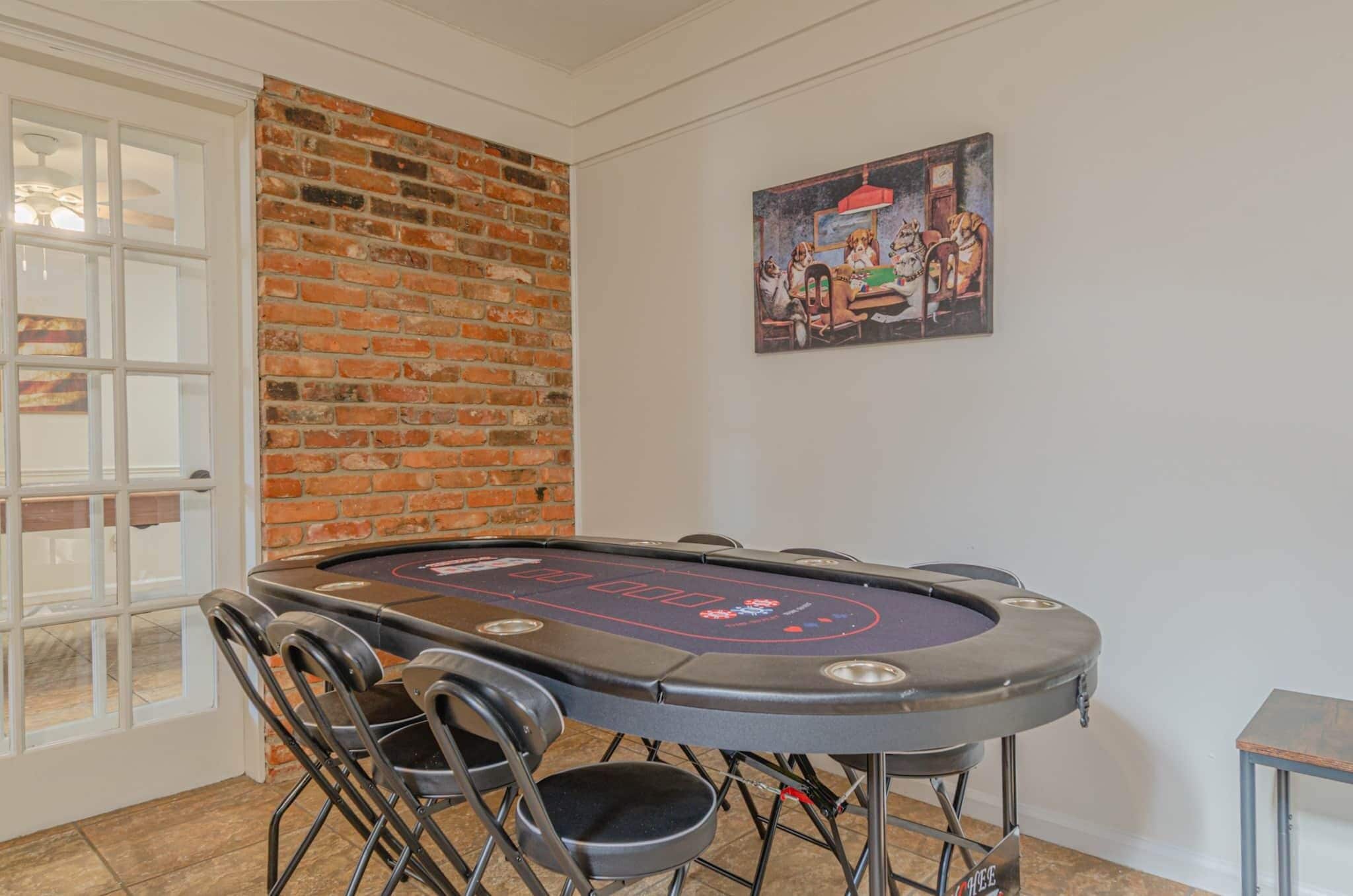 Een pokertafel met stoelen, een bakstenen muur en een schilderij aan de muur.