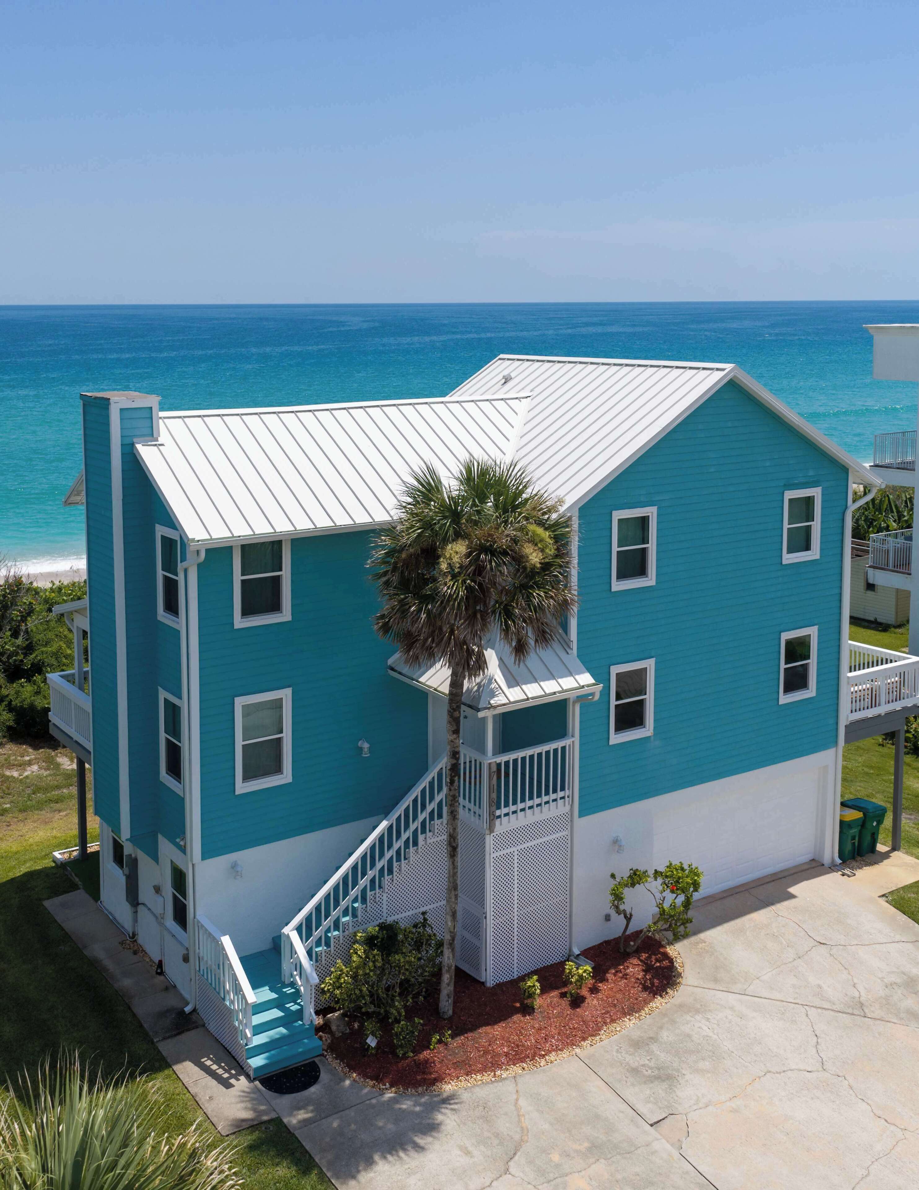 A two-story building with a white roof and teal walls, a staircase, and a view of the ocean.