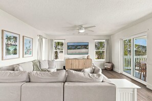 A spacious living room with a large sectional sofa, a wooden cabinet, and a flat-screen TV. - 51 Steps: Beach House w/ Private Beach Access & Deck (Melbourne Beach)