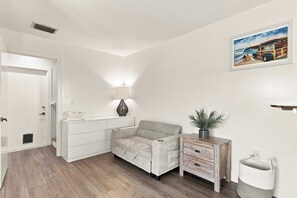 A room with a grey sofa, a white dresser, a lamp, a painting on the wall, and a wooden side table with a plant. - 51 Steps: Beach House w/ Private Beach Access & Deck (Melbourne Beach)