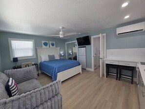 A bedroom with a bed, a desk, a chair, and a TV. - Ocean Whispers at Tuscany Sun: Beach Studio (Melbourne Beach)