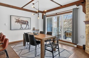 A dining area with a wooden table, black chairs, and a moose painting on the wall. - Cozy Tremblant Escape| Pool & Hot tub (Mont-Tremblant)