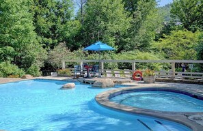 A swimming pool with a hot tub, lounge chairs, and a covered seating area surrounded by trees. - Cozy Tremblant Escape| Pool & Hot tub (Mont-Tremblant)