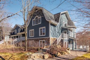 A large, two-story house with a stone facade, multiple windows, and a prominent staircase. - Cozy Tremblant Escape| Pool & Hot tub (Mont-Tremblant)