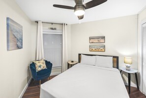 A bedroom with a bed, a chair, a nightstand, a lamp, and a ceiling fan. - Sandcastle Condominium Unit 109 (Port Aransas)