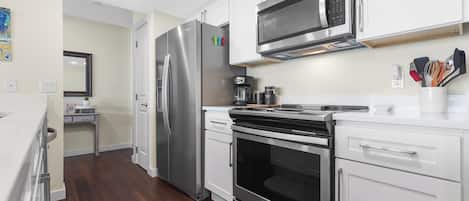 Una cocina moderna con electrodomésticos de acero inoxidable, armarios blancos y piso de madera.