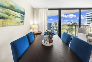 A hotel room with a dining table, blue upholstered chairs, a potted plant, and a view of the beach and buildings. - Sandcastle Condominium Unit 109 (Port Aransas)