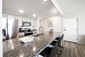 Cocina moderna con electrodomésticos de acero inoxidable, encimeras de granito y una zona de bar con sillas.