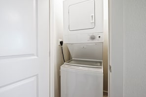 A compact, white, front-loading washer and dryer unit installed in a narrow hallway. - Sandcastle Condominiums Unit 209 (Port Aransas)