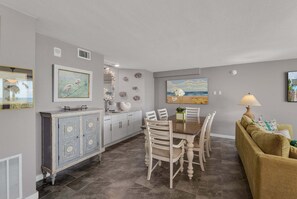 A modern kitchen with a dining area, featuring a marble countertop, white cabinetry, and a dining table with chairs. - Sandcastle Condominiums 321 (Port Aransas)