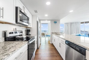 A modern kitchen with stainless steel appliances, white cabinetry, and a view to the outside. - Sandcastle Condominiums 338 (Port Aransas)
