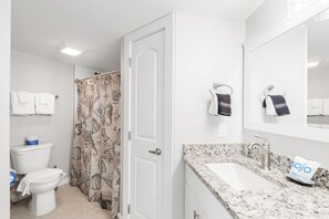 Een badkamer met toilet, douchegordijn, wastafel en handdoekhouders.