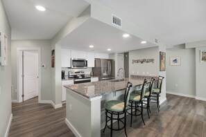 A modern kitchen with a central island, stainless steel appliances, and a bar seating area. - Sandcastle Condominiums 408 (Port Aransas)