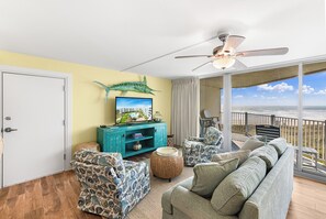 Sala de estar com uma grande janela com vista para o oceano, um ventilador de teto e um rack teal para entretenimento.