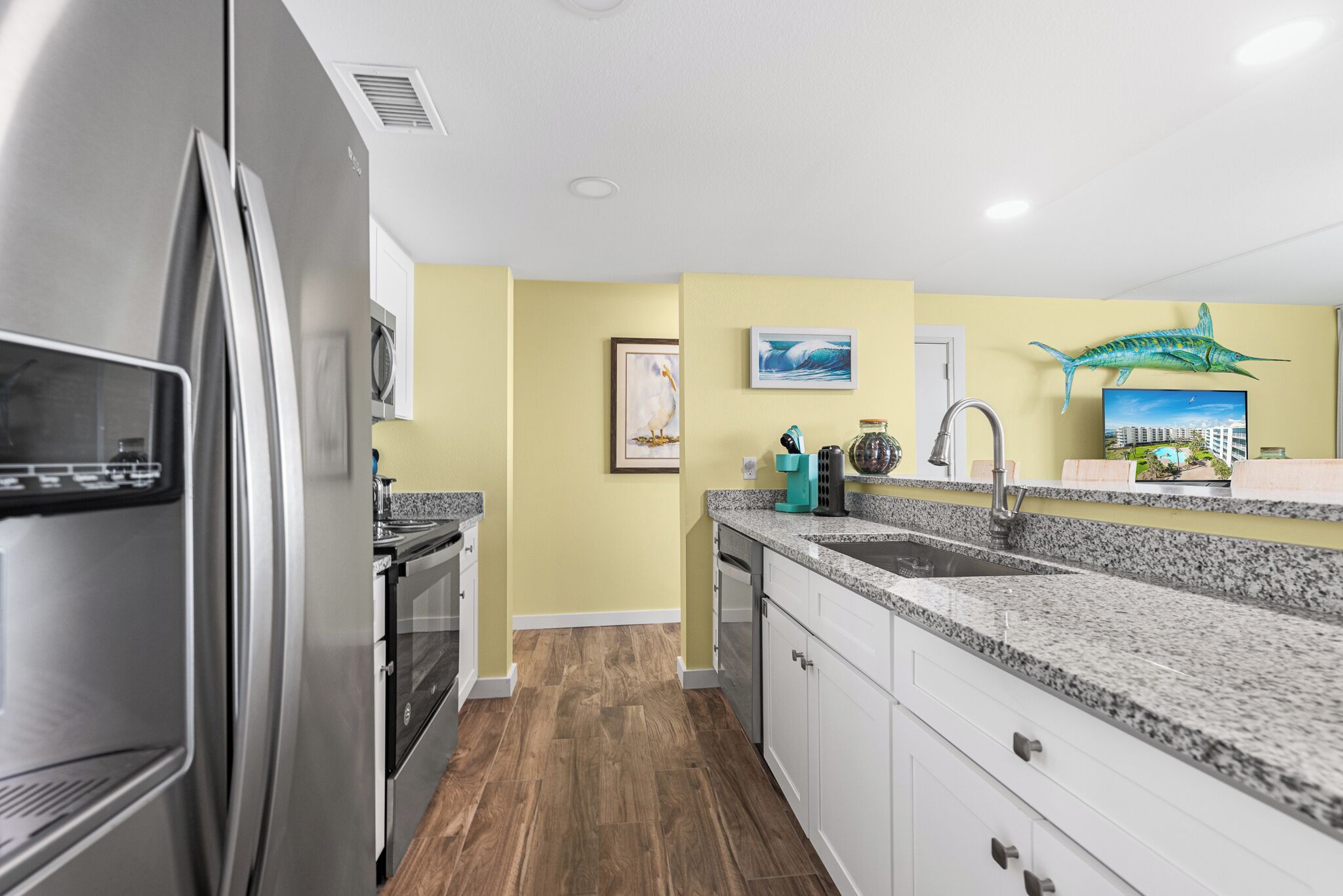 A modern kitchen with a stainless steel refrigerator, granite countertops, and wooden flooring.