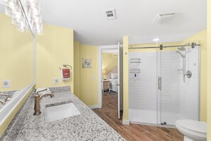 Ein Badezimmer mit Marmorwaschtisch, Toilette, Duschkabine mit Glastür und einem zur Schlafzimmertür führenden Gang.