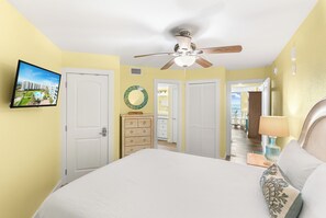 Ein Schlafzimmer mit einem Bett, einem Deckenventilator, einem an der Wand montierten Fernseher und Blick ins Freie.