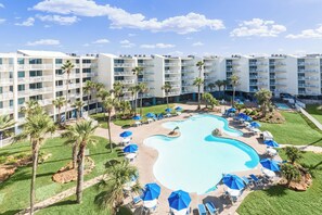 Um hotel com piscina cercada por espreguiçadeiras e guarda-sóis, palmeiras e um edifício de vários andares com varandas.