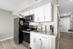 Cozinha moderna com eletrodomésticos de aço inoxidável, armários brancos e bancada de granito.
