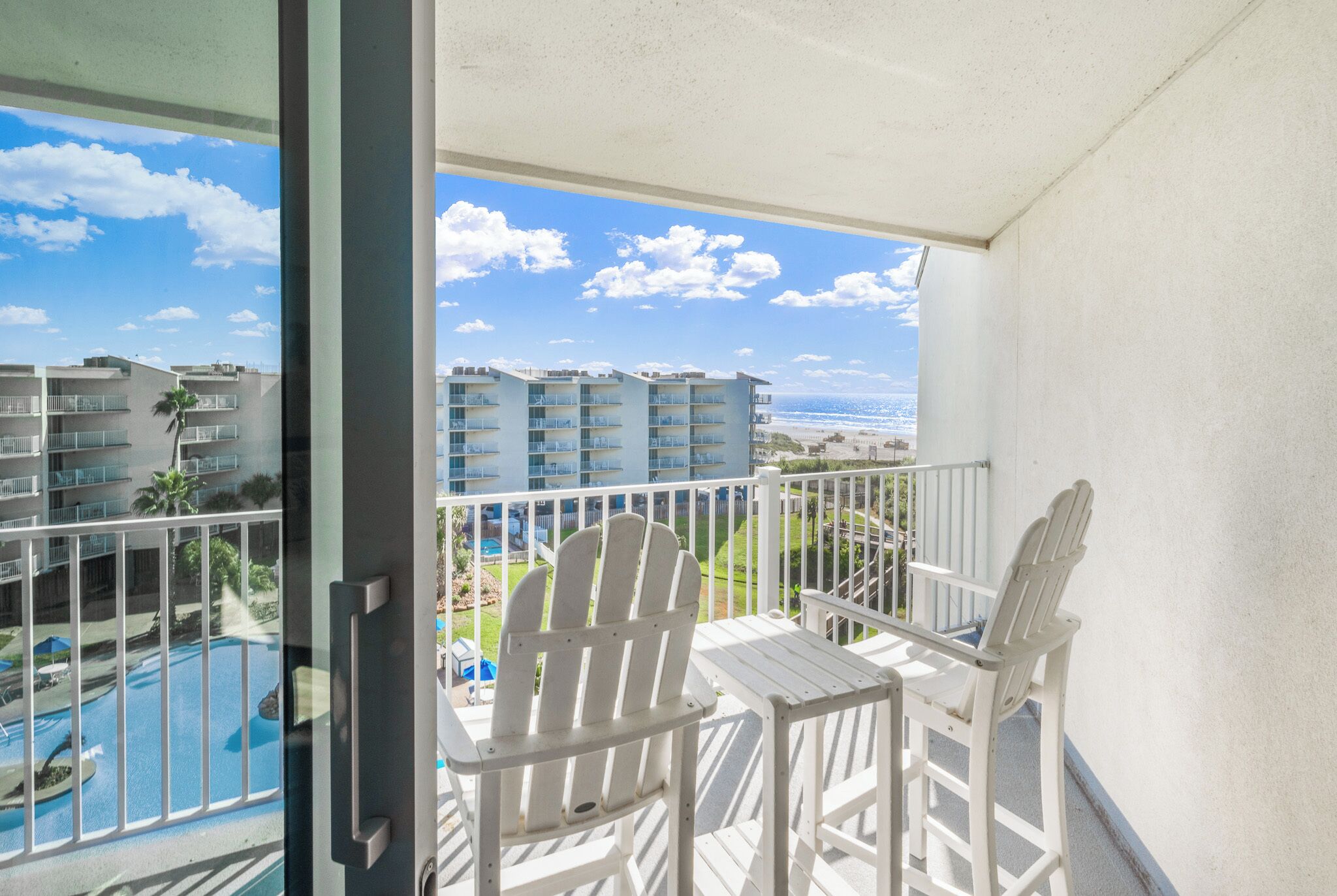 Un balcone con sedie bianche e vista su una piscina e degli edifici.