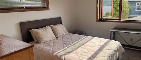 A bedroom with a bed, a desk, and a window.