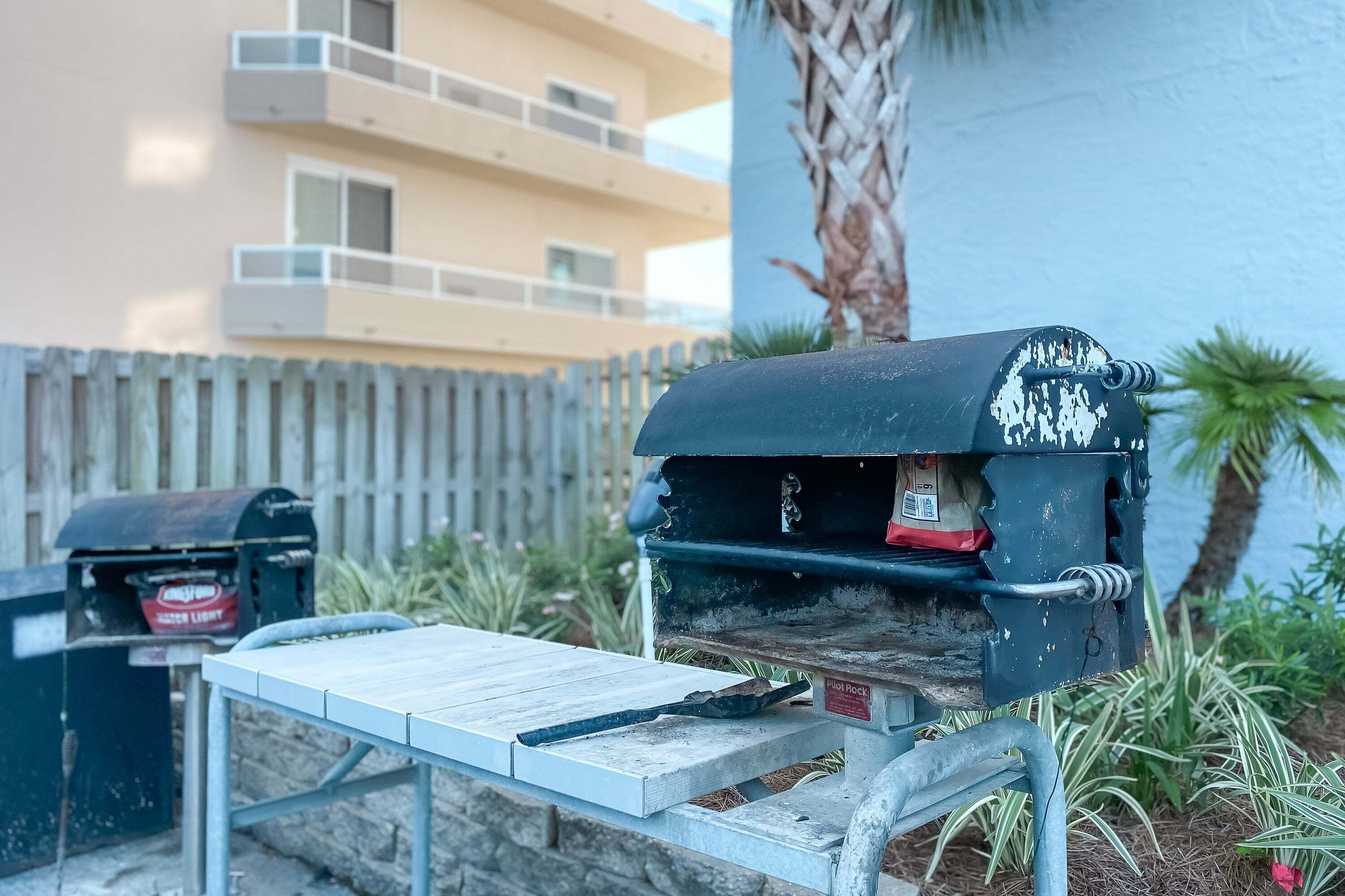 A barbecue grill with a metal table in front, a mailbox, and a building in the background.