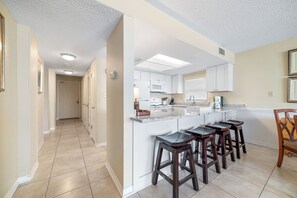 Una cocina moderna con una isla central, taburetes de bar y un comedor con mesa de madera.