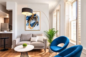 Ein modernes Wohnzimmer mit einer Couch, einem runden Couchtisch, einem blauen Sessel, einer Stehlampe und einem Gemälde an der Wand.