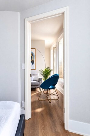 A hallway with a blue chair, a grey sofa, and a plant. - The Penn Hotel -Live Above Gaslamp Nightlife &AC (San Diego)