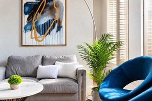 A living room with a grey sofa, a blue chair, a white coffee table, and a green plant. - The Penn Hotel -Live Above Gaslamp Nightlife &AC (San Diego)