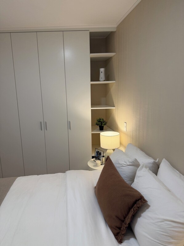 A bedroom with a bed, pillows, a nightstand, a lamp, a shelf with a plant, and a wardrobe. - Vrbo Property (Jesús María)