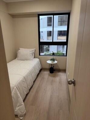 A small, narrow room with a bed, a window, and a small table with a plant. - Vrbo Property (Jesús María)