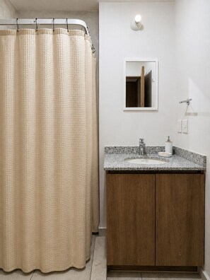 Een badkamer met douchegordijn, wastafel met spiegel en houten kasten.