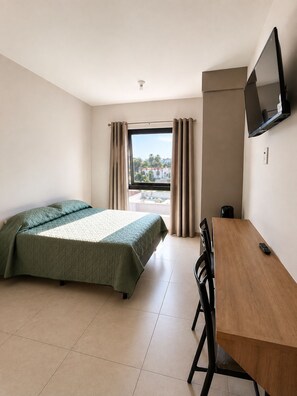 Hotelkamer met een bed, bureau, stoel, televisie aan de muur en raam met gordijnen.