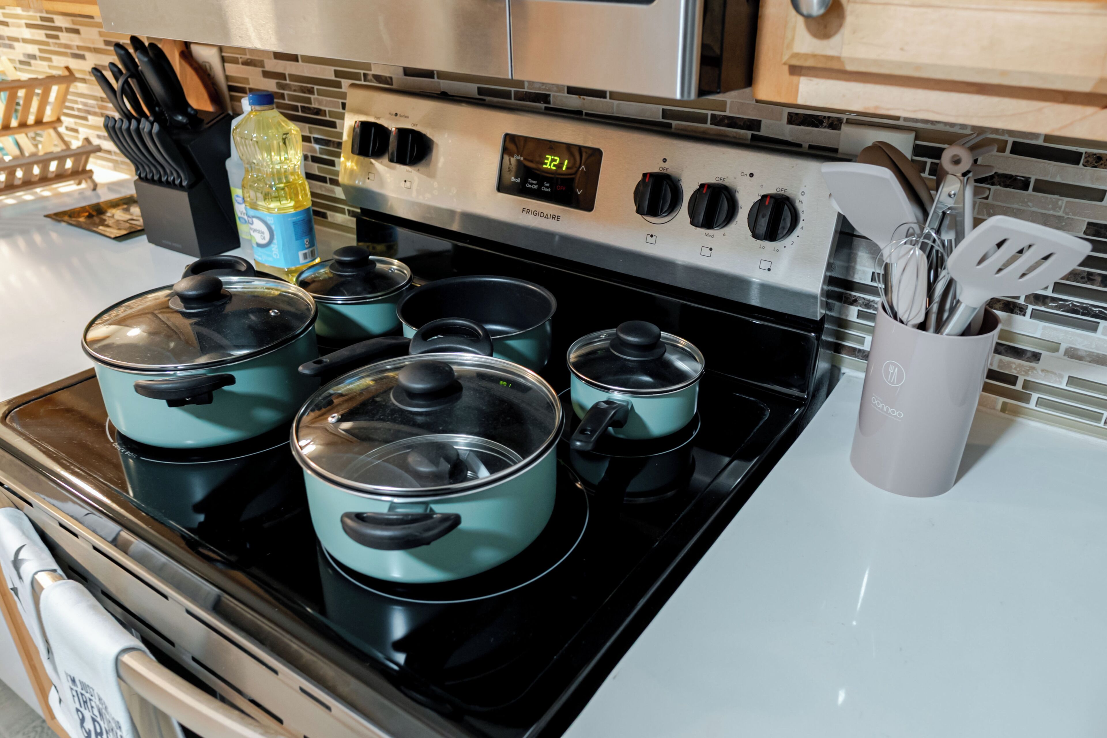 Una cocina con estufa, ollas, una botella de detergente para platos y un recipiente para utensilios.